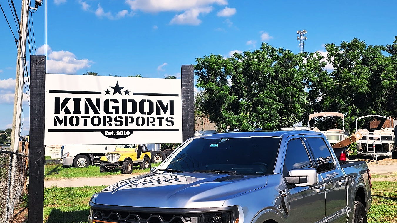 Gray Ford F-150 parked beside the KINGDOM MOTORSPORTS roadside sign on the lot, RVs and golf carts behind